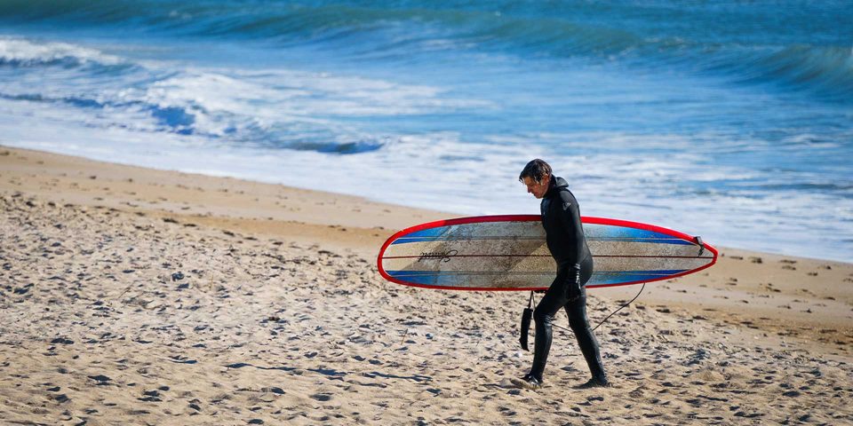 Man in wetsuit carrying surfboard on a North Carolina beach